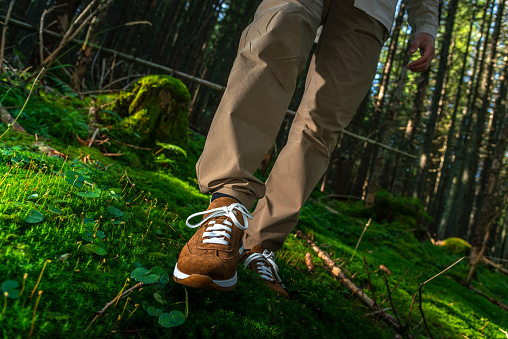 Young male walking on moss wearing brown suede sneakers in the dense forest