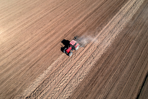 Aerial view of a red tractor plowing field with a harrow in spring.