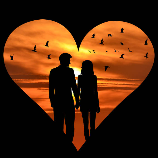 Heart shape with lovers silhouettes and flying birds over sunset sky