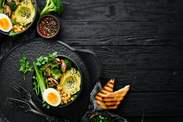 istock Buddha bowl: avocado, chickpeas, mushrooms, egg and arugula in a black bowl. Top view. Free space for text. 1972371250
