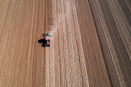 Aerial view of a red tractor plowing field with a harrow in spring.