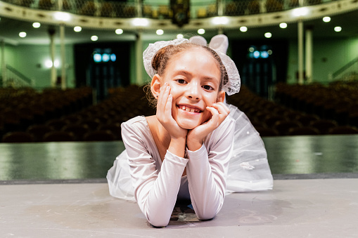 Portrait of a child ballerina lying down on stage theater