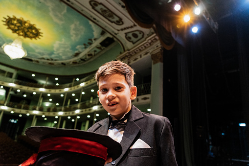 Portrait of a child magician boy doing magics at stage theater