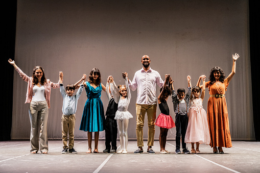 Portrait of parents and children thanking the audience after performance at stage theater