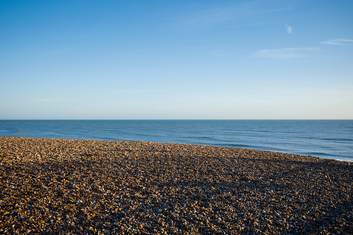 An empty pebble beach with a sea horizon on a sunny day.