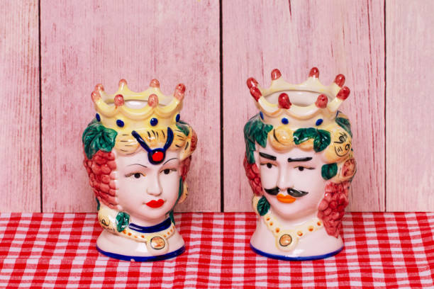 souvenir from sicily. traditional sicilian ceramic pots or vases with heads of a couple of lovers of moorish heads on red checked napkin of wooden wall. - heath ceramics fotografías e imágenes de stock