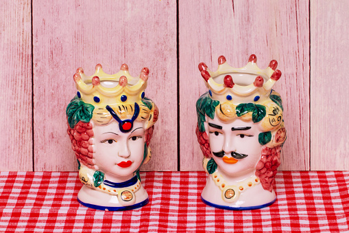 Souvenir from Sicily. Traditional sicilian ceramic pots or vases with heads of a couple of lovers of Moorish heads on red checked napkin of wooden wall.