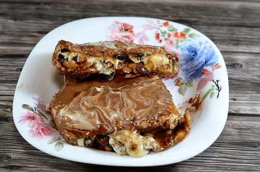 A pie baked dough covered with chocolate sauce and stuffed with pieces of chocolate, biscuit pieces, banana, cake, caramel and chocolate hazelnut cream spread and sauce, a chocolate sweet pastry, selective focus