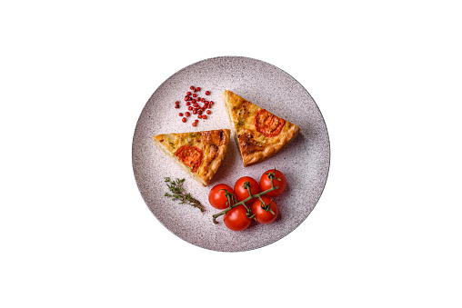 Delicious quiche with tomato, cheese, chicken, spices and herbs on a dark concrete background