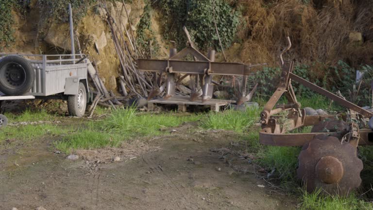 Old abandoned rusty farming equipment next to field with garden.