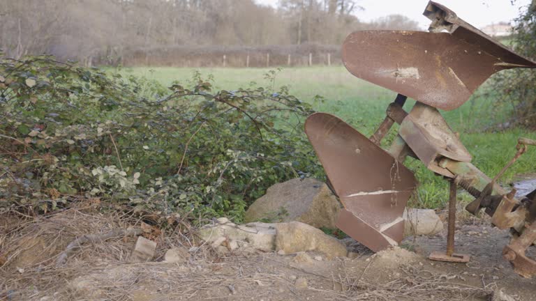 Old abandoned rusty farming equipment next to field with garden.