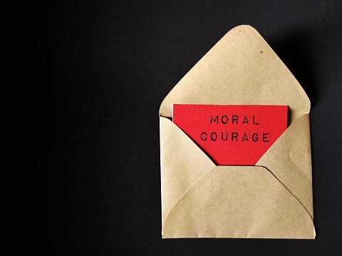Craft envelope on black background with text on red card MORAL COURAGE, means courage to take action for moral reasons or act upon ethical values to help others during difficult ethical dilemmas