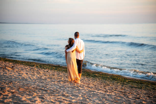 An attractive couple walking and hugging on the beach, under the blue sky