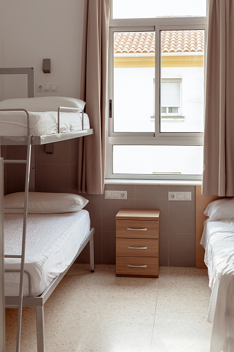A clean and minimalistic hostel room with a bunk bed, white bedding, and a small wooden bedside table, ideal for budget travelers seeking affordable accommodation. Cheap hostels, save money
