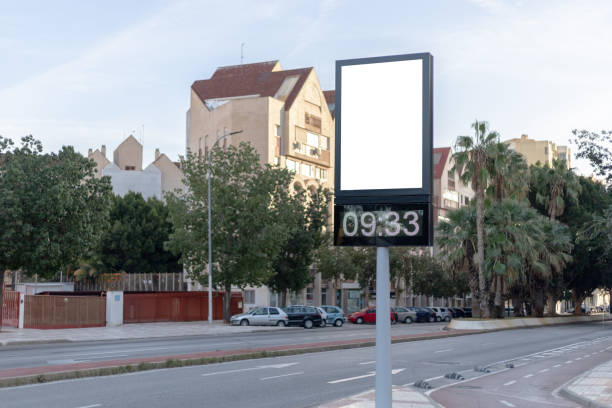 istock Urban digital clock post with a blank advertising panel against a cityscape, ideal for promotions. Vertical billboard mockup, empty display. Copy space for text, picture. 1972456598