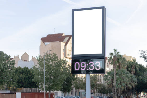Urban digital clock post with a blank advertising panel against a cityscape, ideal for promotions. Vertical billboard mockup, empty display. Copy space for text, picture.