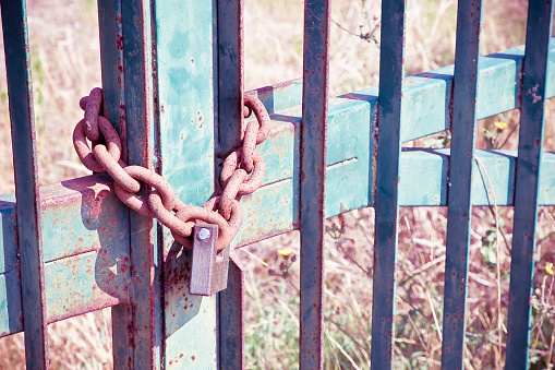 Old damaged and rusty metal gate of a factory closed with padlock - Factory shut down concept