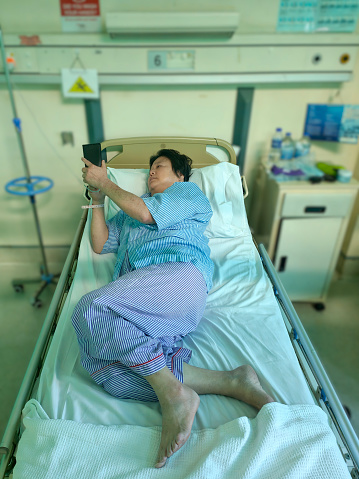 An Asian woman is using smartphone while admitted into hospital