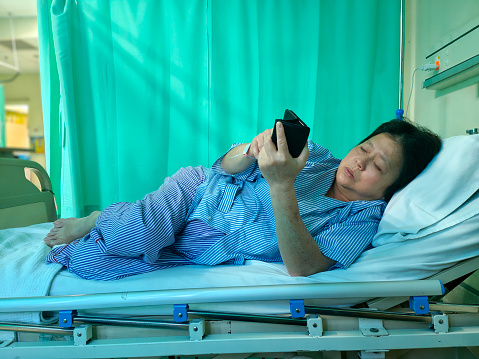 An Asian woman is using smartphone while admitted into hospital