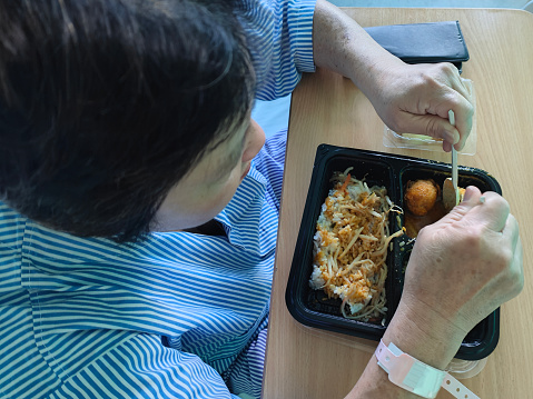 An Asian woman is enjoying lunch while admitted into hospital