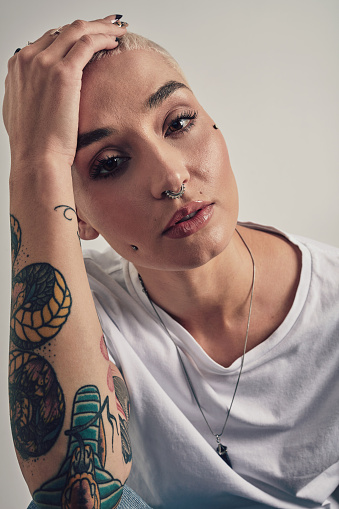 Tattoo, piercing and portrait of woman with beauty in grey background of studio with confidence. Unique, girl and person with edgy, punk or grunge aesthetic for makeup and ink on body with pride