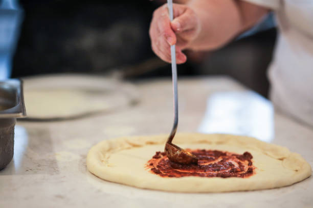 istock Chef Preparing Pizza In The Kitchen, Applying Pizza Sauce To The Dough 1972499074