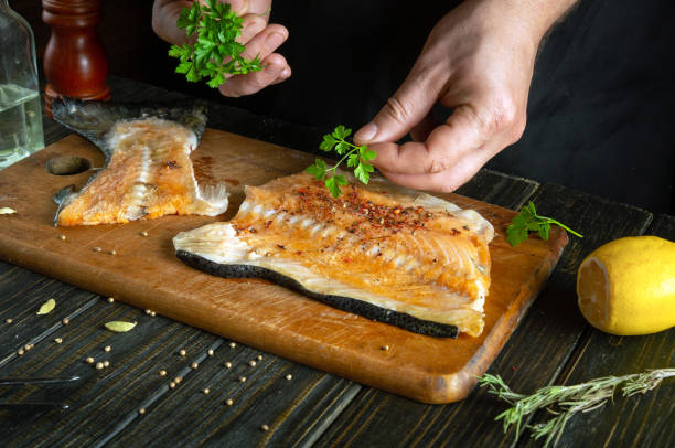 istock We prepare fresh red fish in the restaurant kitchen before salting with aromatic spices. Chef hand adding parsley to fish steak 1972503848