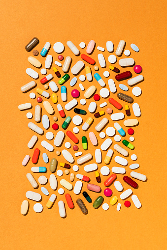Colorful pills on orange background, directly above medical background