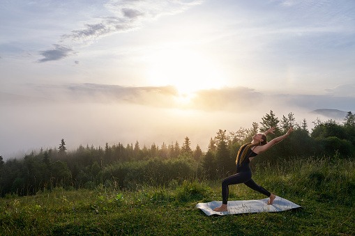 Young woman with slender body having yoga practice during morning time outdoors. Active female person with braids training regularly on fresh air during summer time.