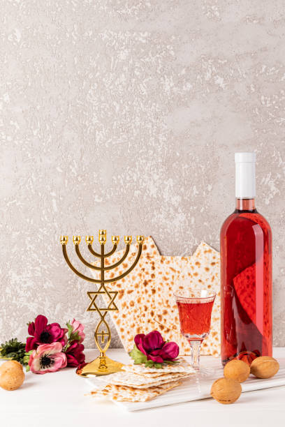 праздничная композиция к еврейской пасхе. бутылка кошерного вина, маца, хрустальный бокал вина, традиционная менора из золотого подсвечник - passover matzo wine wine bottle стоковые фото и изображения