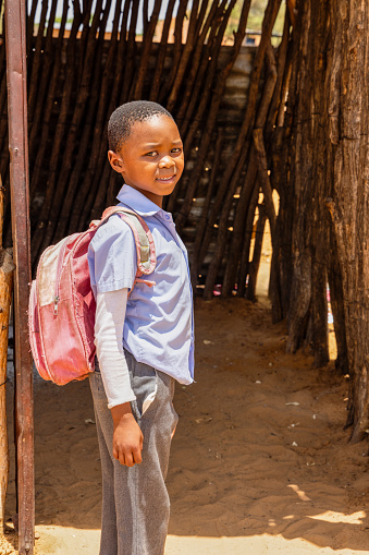 village poor african boy with a backpack wearing an uniform going to school