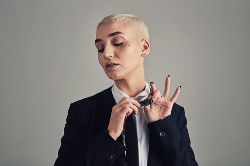 Fashion, suit and tie with business woman dressing in studio on gray background for business or formal style. Elegant, classy or trendy with edgy young non binary person getting ready for work