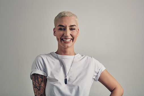 Smile, portrait and woman with tattoo fashion, alternative culture and casual confidence in studio. Happy face of gen z girl with creative identity style, trendy clothes and pride on grey background.