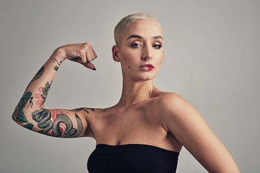 Portrait, flexing arms and woman with empowerment, winner and motivation on a grey studio background. Face, person and model show strength, freedom and winner with style and tattoo with confidence