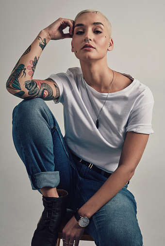Chair, portrait and woman with tattoo style, alternative culture or streetwear in studio. Artistic entrepreneur with creative identity, fashion and trendy clothes with pride on grey background