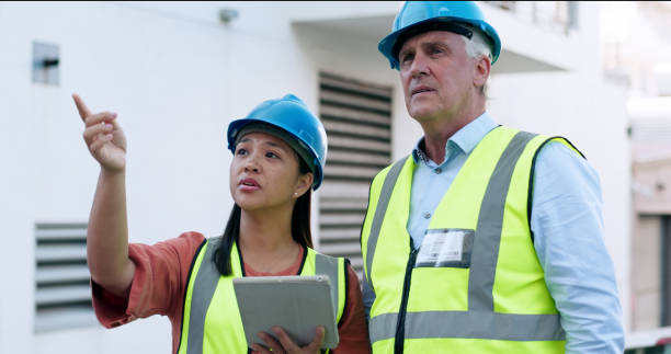 istock Construction, team and tablet for inspection with people at job site, mentor and apprentice with communication. Architecture, engineering and digital floor plan, old man and woman outdoor in meeting 1972558561
