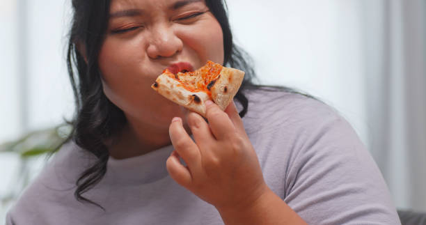 istock A chubby Asian woman enjoying pizza while relaxing on the sofa at home. 1972577826