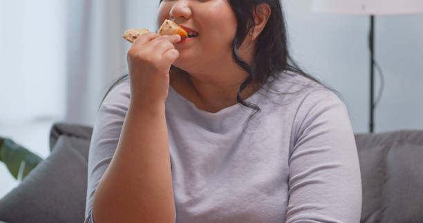 istock A chubby Asian woman enjoying pizza while relaxing on the sofa at home. 1972577829