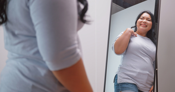 A chubby Asian woman feels confident and proud of her body while standing in front of the mirror.