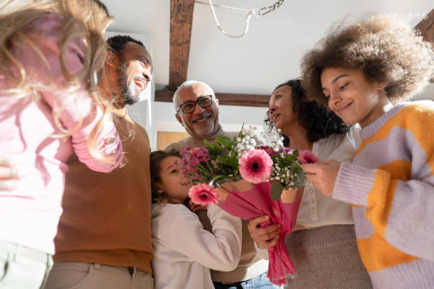 Happy diverse family gathering with flowers for the grandparents. Infoors.
