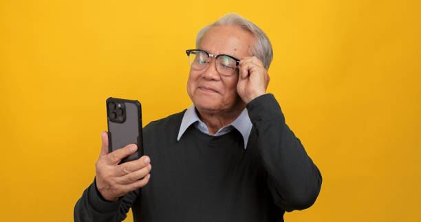 istock Asian old man using smart phone. Isolated on yellow background in the studio. 1972578947
