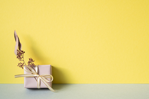 Purple gift box with dry flower on gray table. yellow wall background