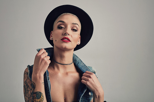 Style, makeup and portrait of woman in a studio with stylish, grunge and cool outfit with hat. Cosmetic, tattoos and young female person with edgy and trendy fashion and accessory by gray background.
