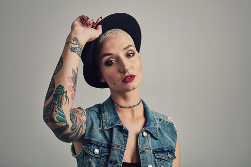Fashion, makeup and portrait of woman in a studio with stylish, grunge and cool outfit with hat. Cosmetic, tattoos and young female person with edgy and trendy style and accessory by gray background.