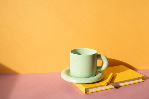 Notebook and colored pencil, coffee cup on pink desk. orange wall background. workspace