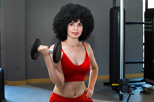 Brunette woman in red sportswear holds heavy dumbbells in her hands during training.