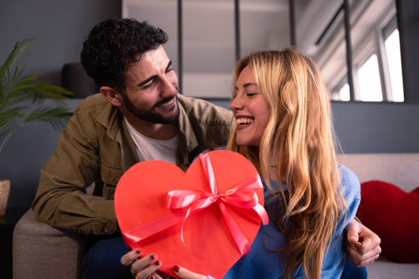 istock Young couple looking lovingly at each other smiling with heart-shaped gift box. Valentine's Day Celebration. 1972609696