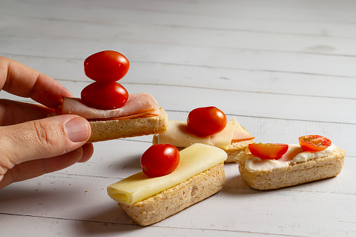 A hand picks up a piece of bread with tomato, cheese, and ham. The mini buns or bread rolls – in Brazil, they are called 'Bisnaguinha.