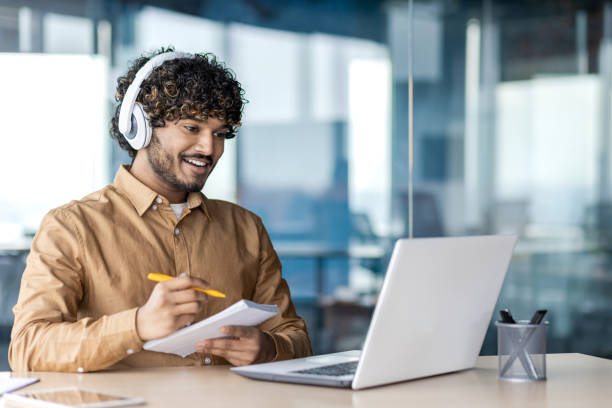 istock Businessman is studying inside the office, man is upgrading his qualifications, watching online video course, recording data, worker in headphones, talking, using video call 1972662820