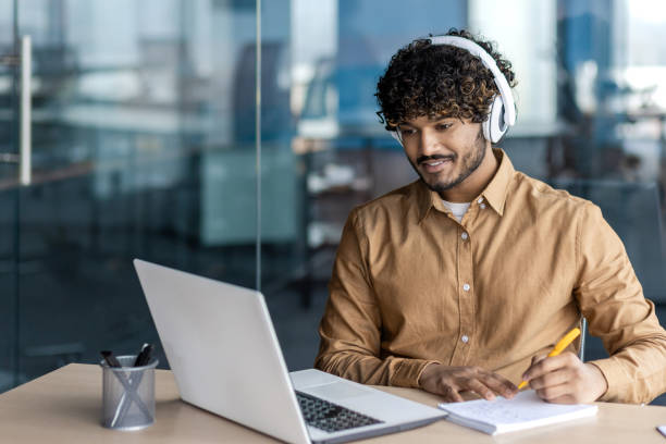 istock Businessman is studying inside the office, man is upgrading his qualifications, watching online video course, recording data, worker in headphones, talking, using video call 1972663070